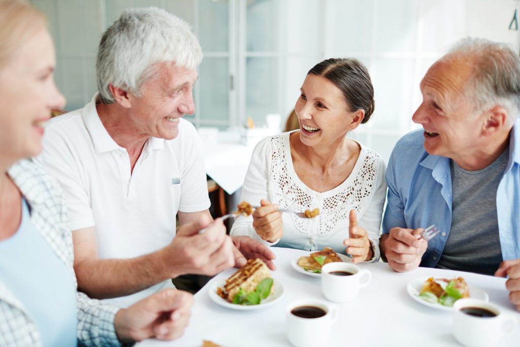 Cheerful senior friends having tasty dessert and talking in shared dining room