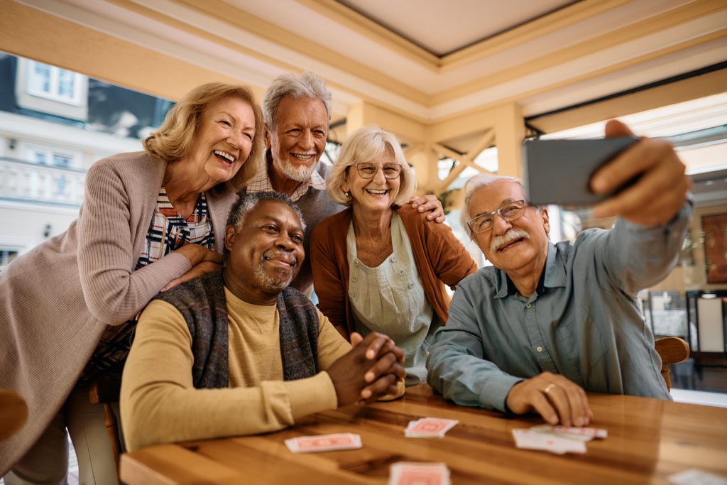 Multiracial group of happy senior people taking selfie with cell phone in assisted living home.