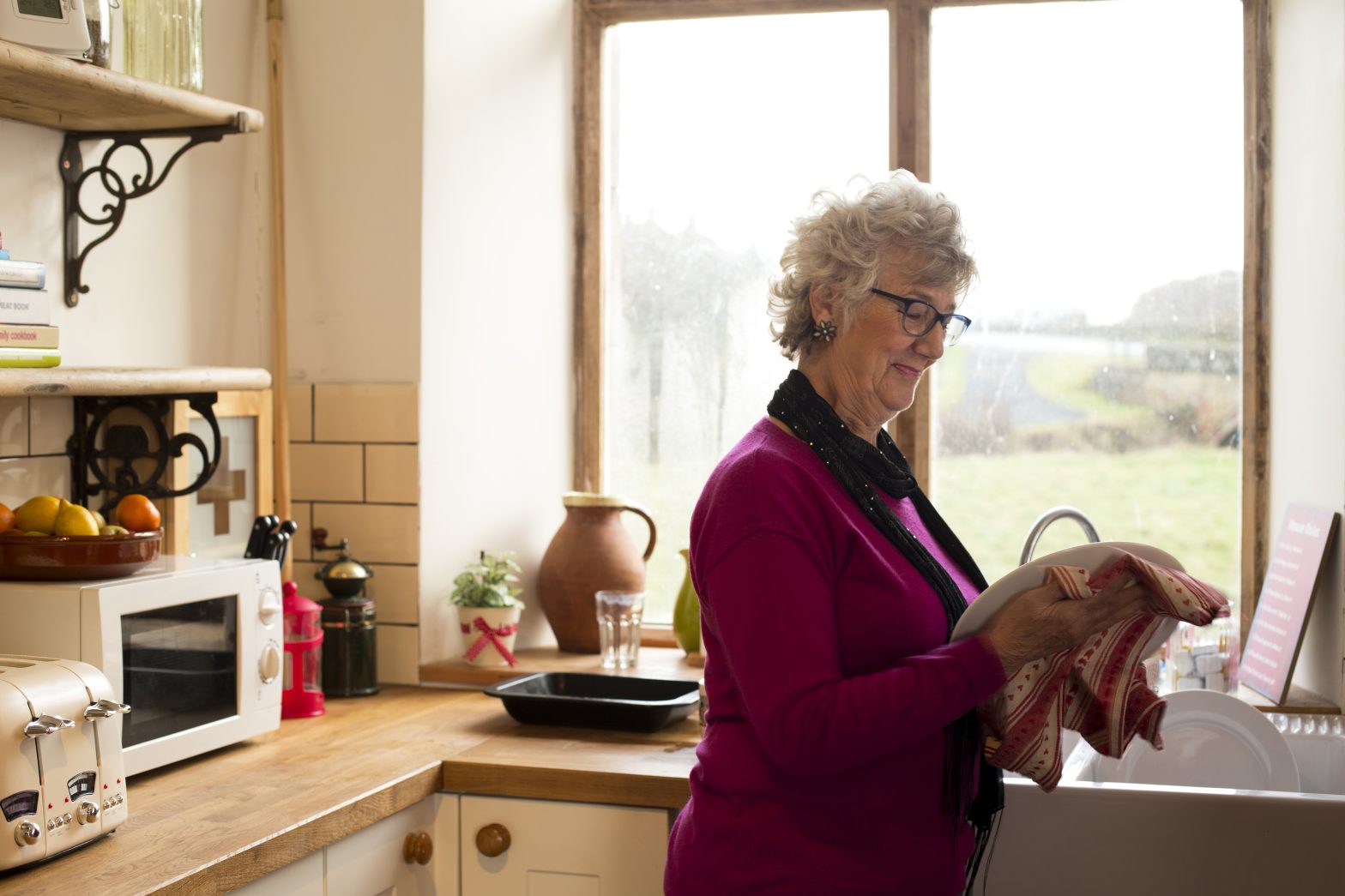 A woman in an independent living apartment in a kitchenette, drying dishes.