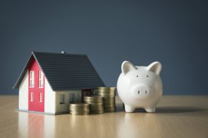A piggy bank and some coins next to a house, representing affordable independent living for seniors.
