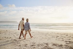Retiree couple walking along a white-sand beach on Alabama's Gulf Coast on a sunny day.