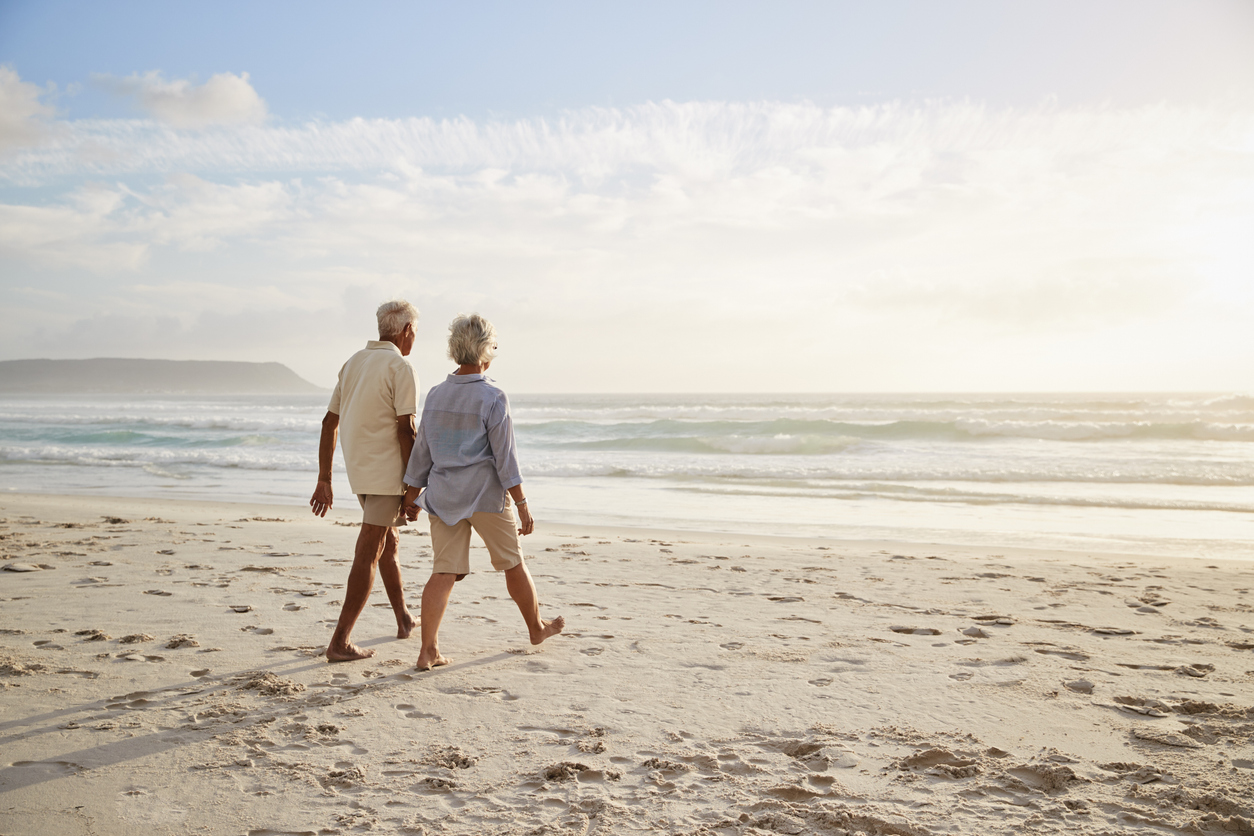 Retiree couple walking along a white-sand beach on Alabama's Gulf Coast on a sunny day.