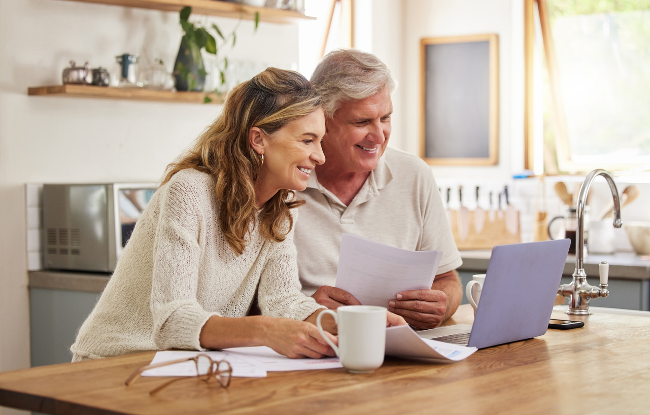 Active older couple reviewing financial documents together at a bright kitchen table, smiling and planning for retirement