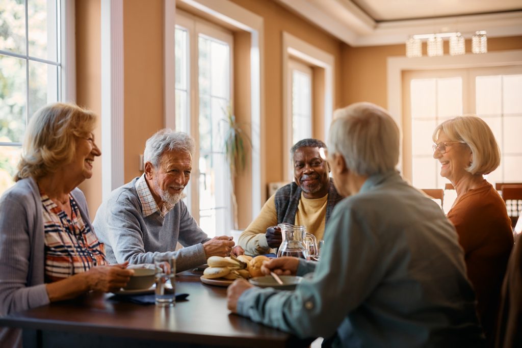 A group of independent living seniors gather around a dining table, enjoying a meal together.