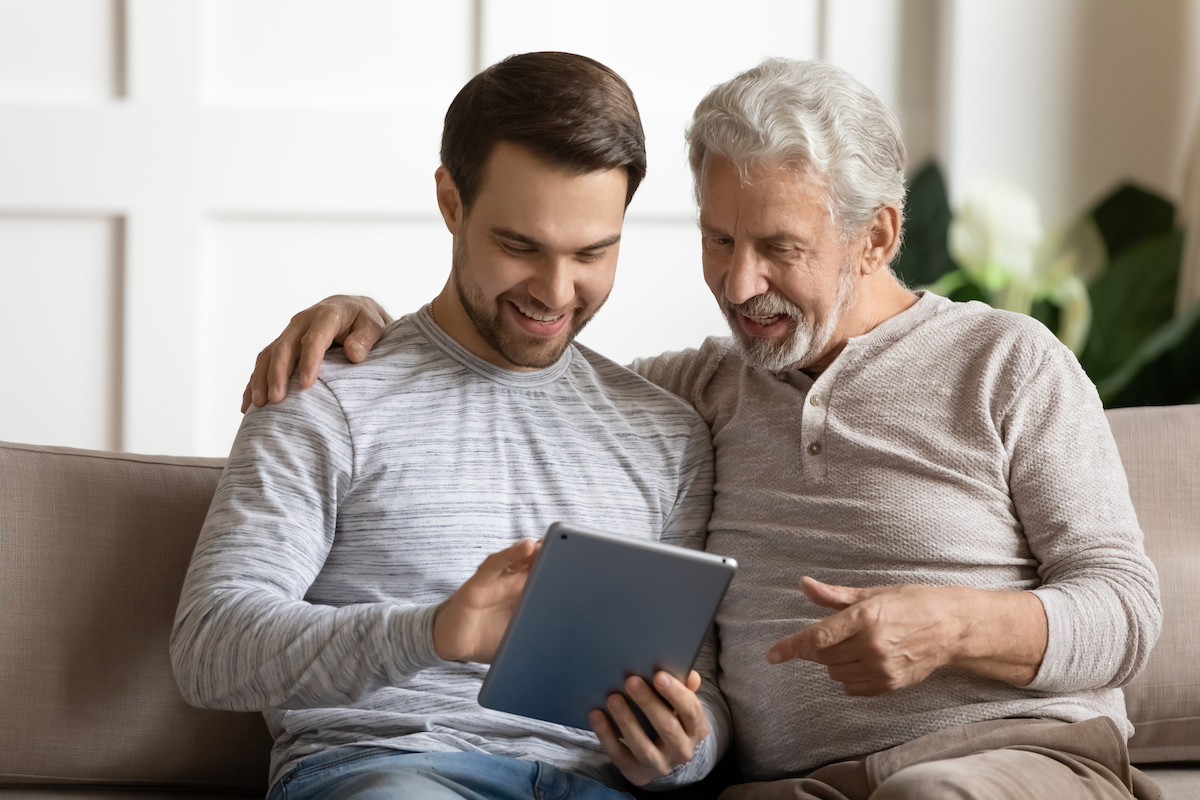 Senior and Adult Son Sit on Couch and Look at Tablet_Community Senior Life