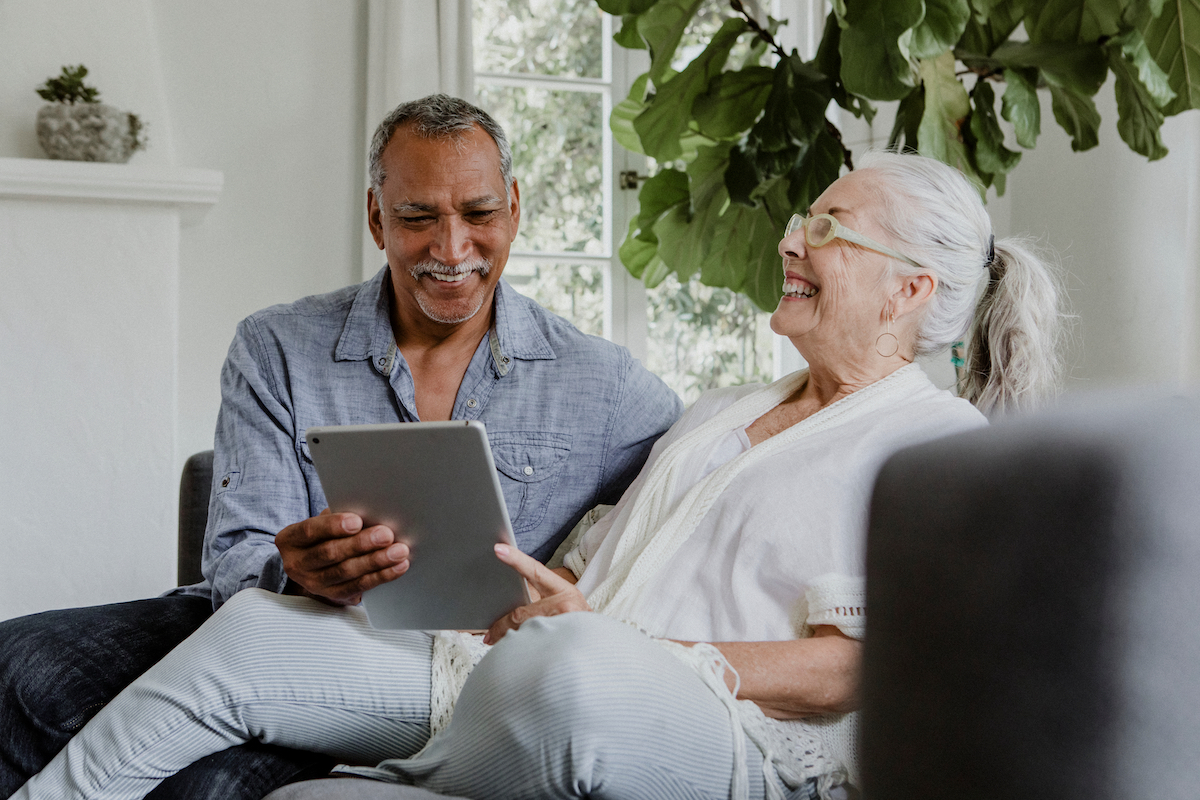 Happy senior couple using tablet on couch_Community Senior Life