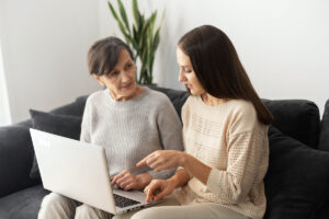 Senior Woman and Daughter Sitting on Couch Looking at Laptop_Community Senior Life