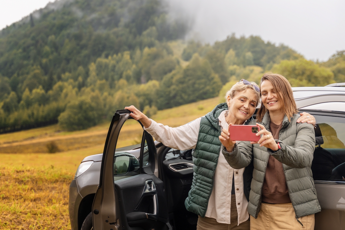 Senior Woman and Adult Daughter Take Selfie Next to Vehicle_Community Senior Life